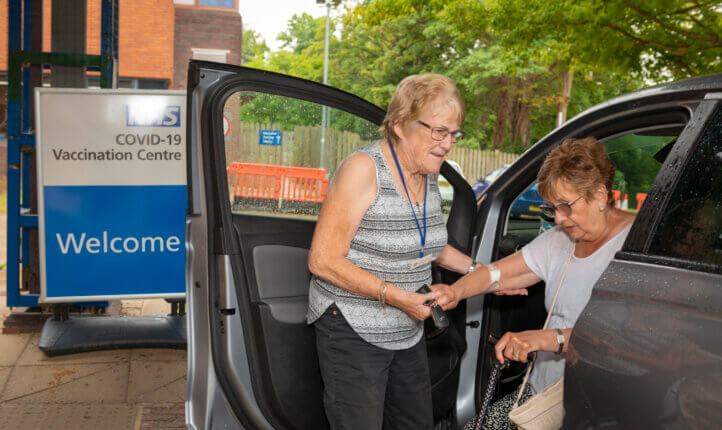 A volunteer helping a disabled lady out of a car